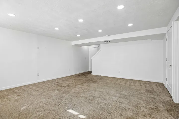 Neutral carpet flooring, recessed ceiling lighting, bright white walls, white trim, and a white interior door