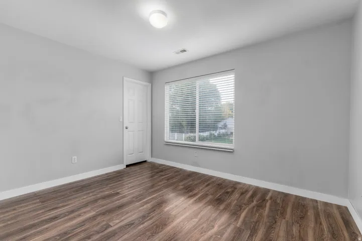 Wood-finish flooring, neutral wall tones, window with blinds, white trim, and a flush mount ceiling light