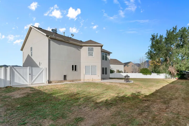 Expansive backyard with a hardscaped patio, fire pit, and white privacy fencing