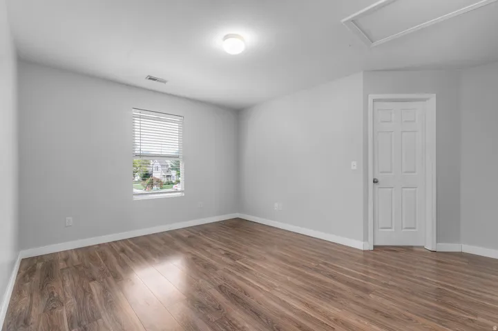 Wood-finish flooring, neutral wall tones, single window with blinds, overhead lighting fixture, and a paneled door