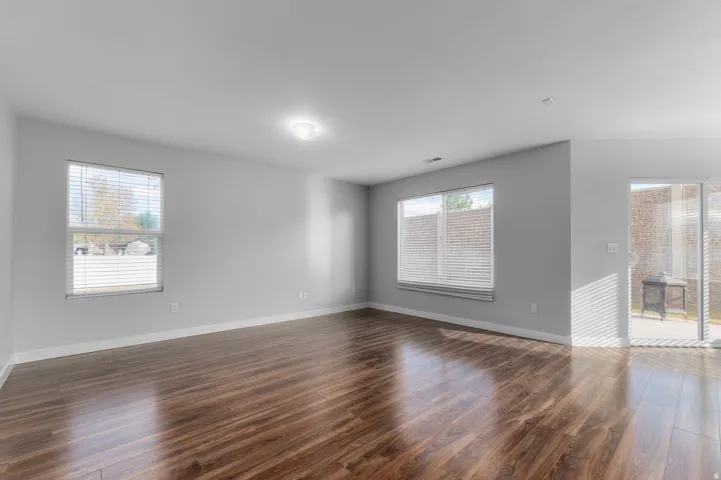 Wood-finish flooring, light grey wall paint, two windows with blinds, recessed ceiling lighting, and a sliding glass door
