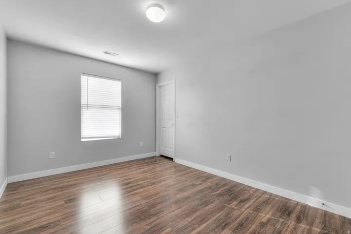Wood-finish flooring, neutral wall tones, window with horizontal blinds, flush mount ceiling light, and a white interior door