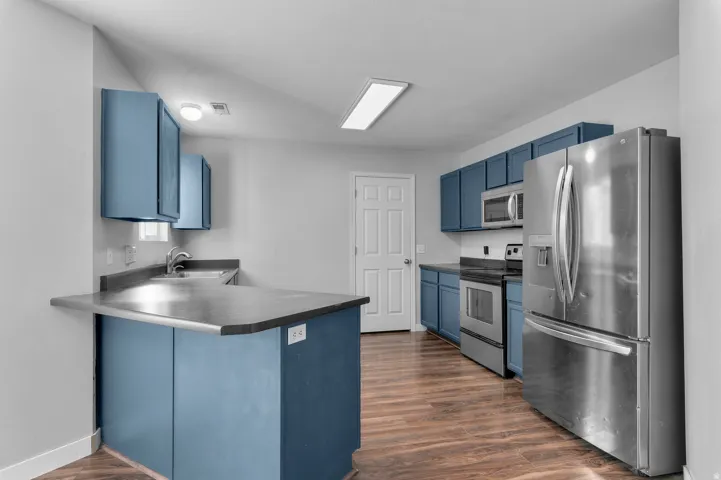 Kitchen featuring blue cabinetry, stainless steel appliances, dark countertops, wood-finish flooring, and a breakfast bar