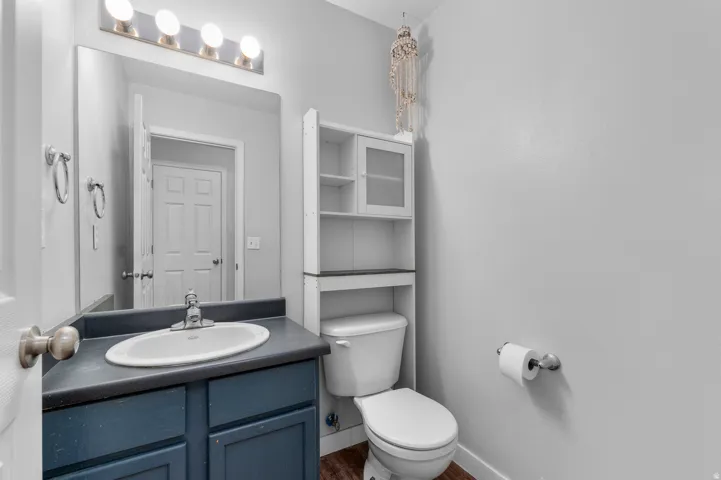 Vanity with a dark countertop and undermount sink, overhead light fixture, toilet, and built-in shelving with glass-fronted cabinets