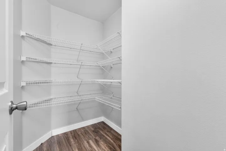 Corner pantry with multiple wire shelving units, wood-finish flooring, and white baseboards