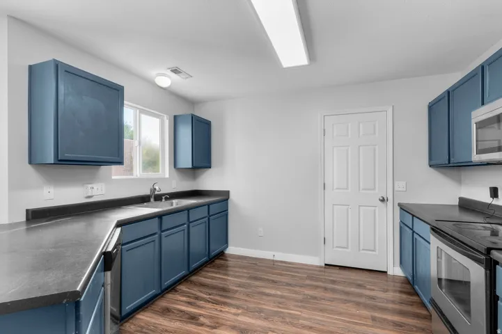 Kitchen featuring wood-finish flooring, blue cabinetry, dark countertops, a stainless steel sink, and a built-in microwave