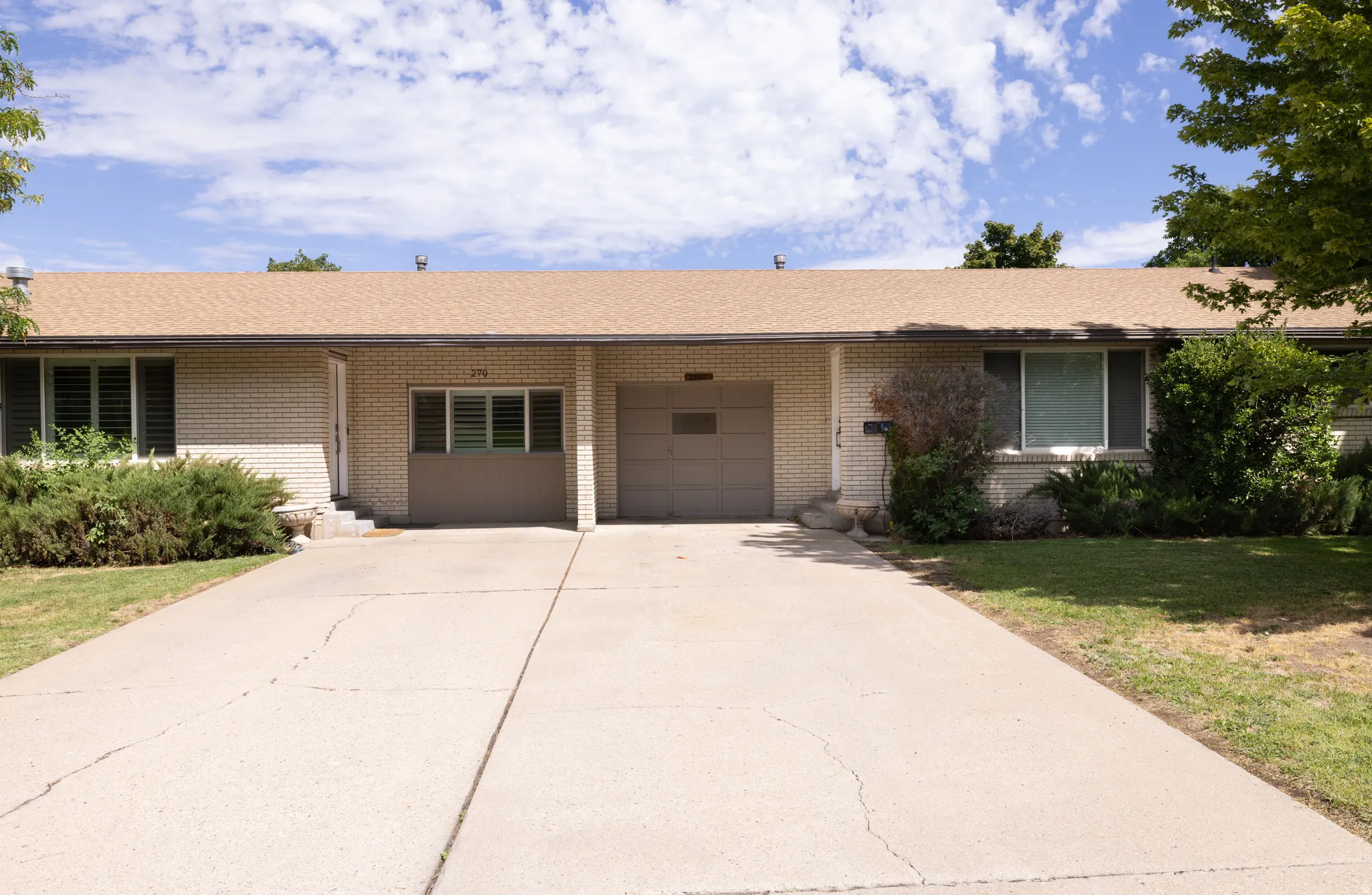 Light brick exterior with a brown shingle roof, integrated garage, and a concrete driveway