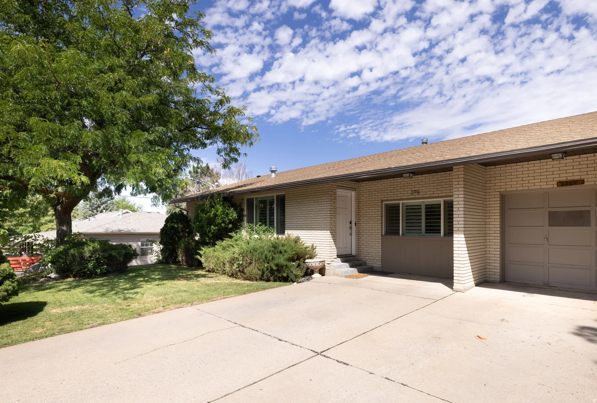 Brick exterior with an attached garage, paved driveway, and mature landscaping