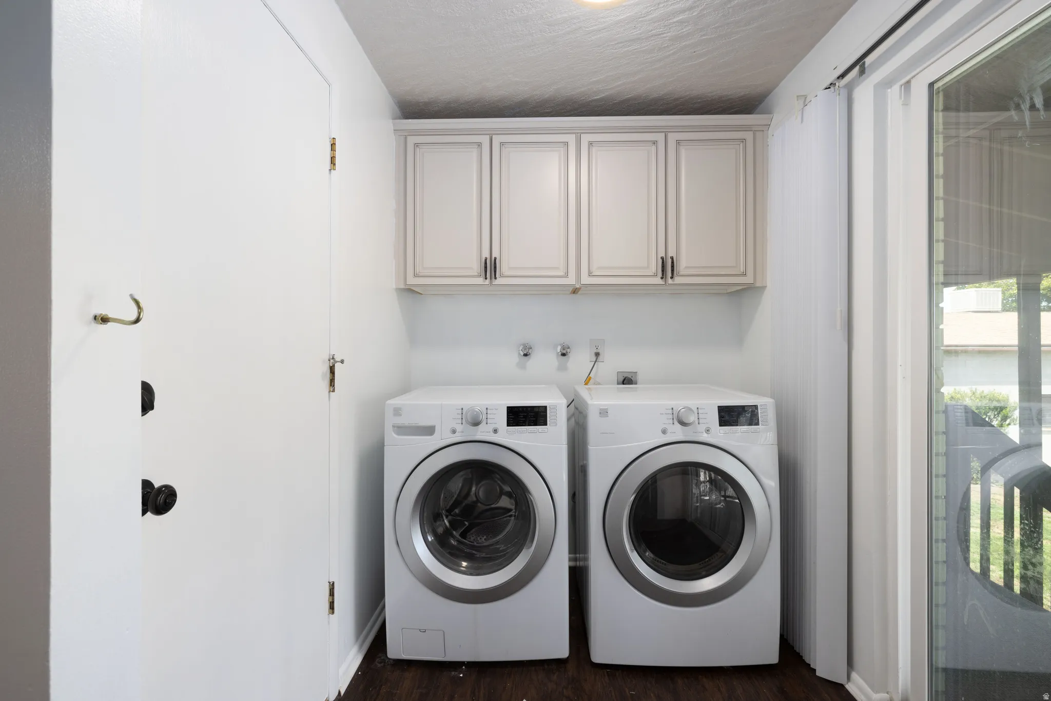 Laundry area featuring upper cabinetry, dark wood-finish flooring, and a sliding glass door