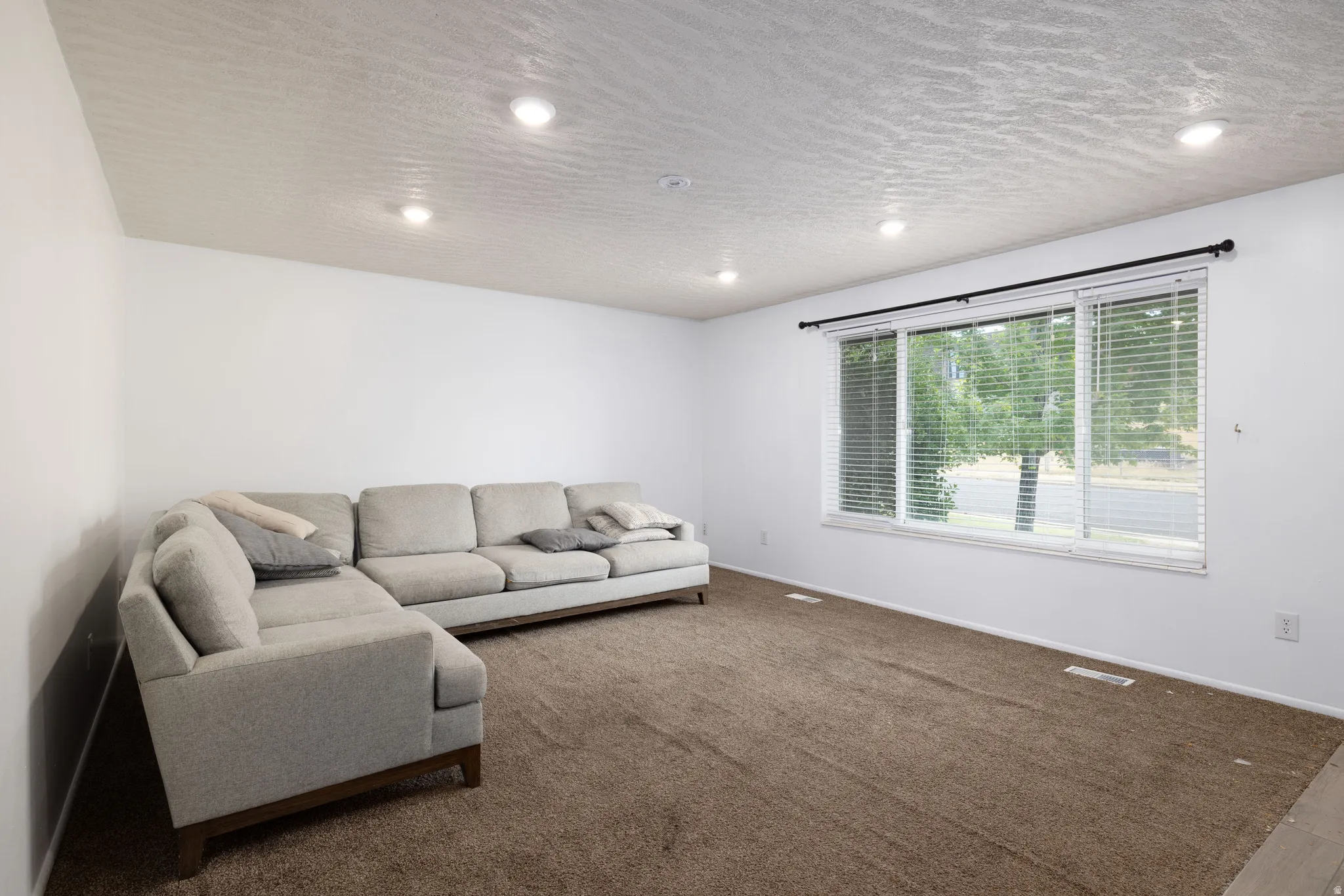 Recessed ceiling lighting, textured ceiling, expansive window with horizontal blinds, and wall-to-wall carpeting