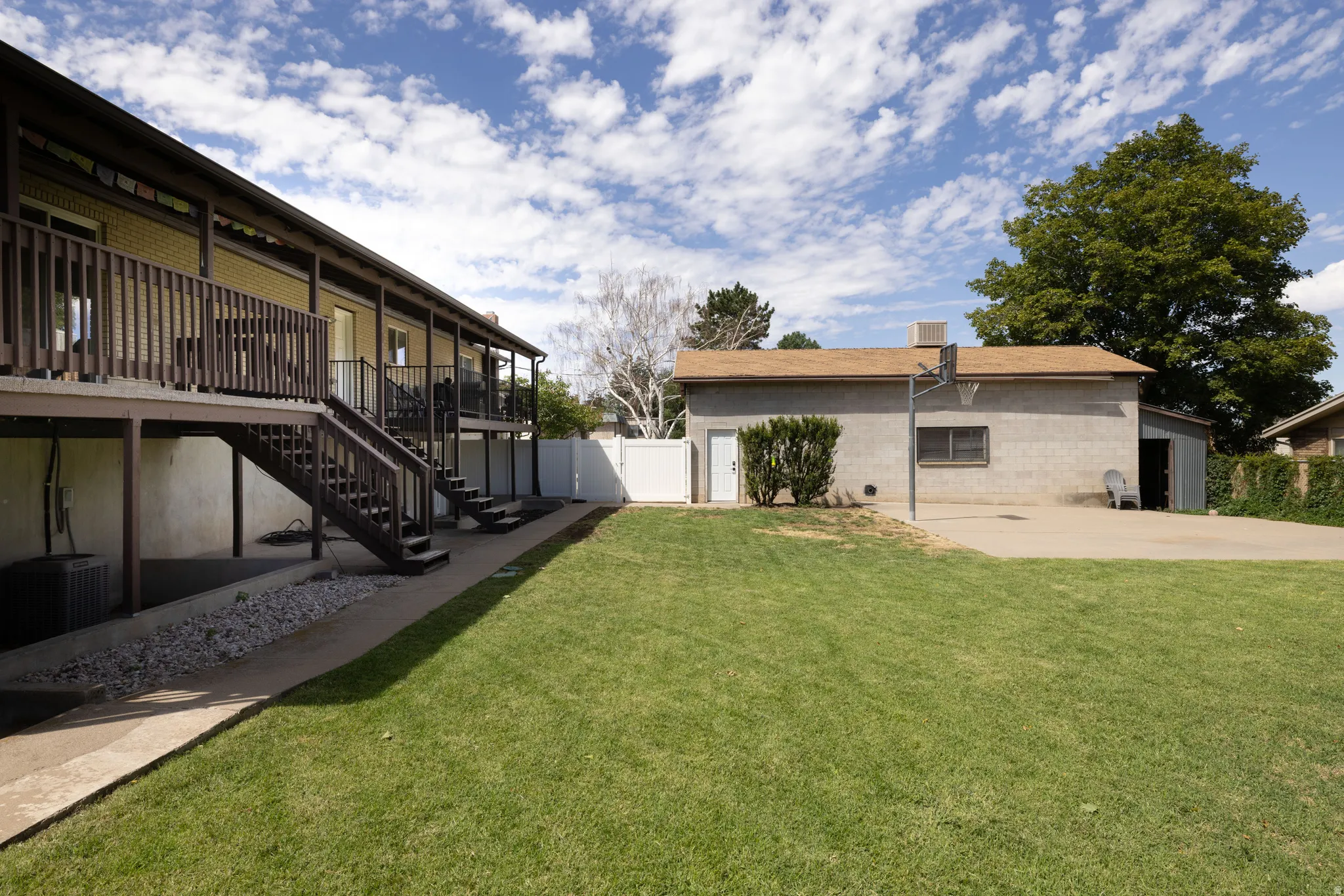 Expansive backyard featuring a manicured lawn, multi-level deck with wood railings, and a detached structure with a basketball hoop