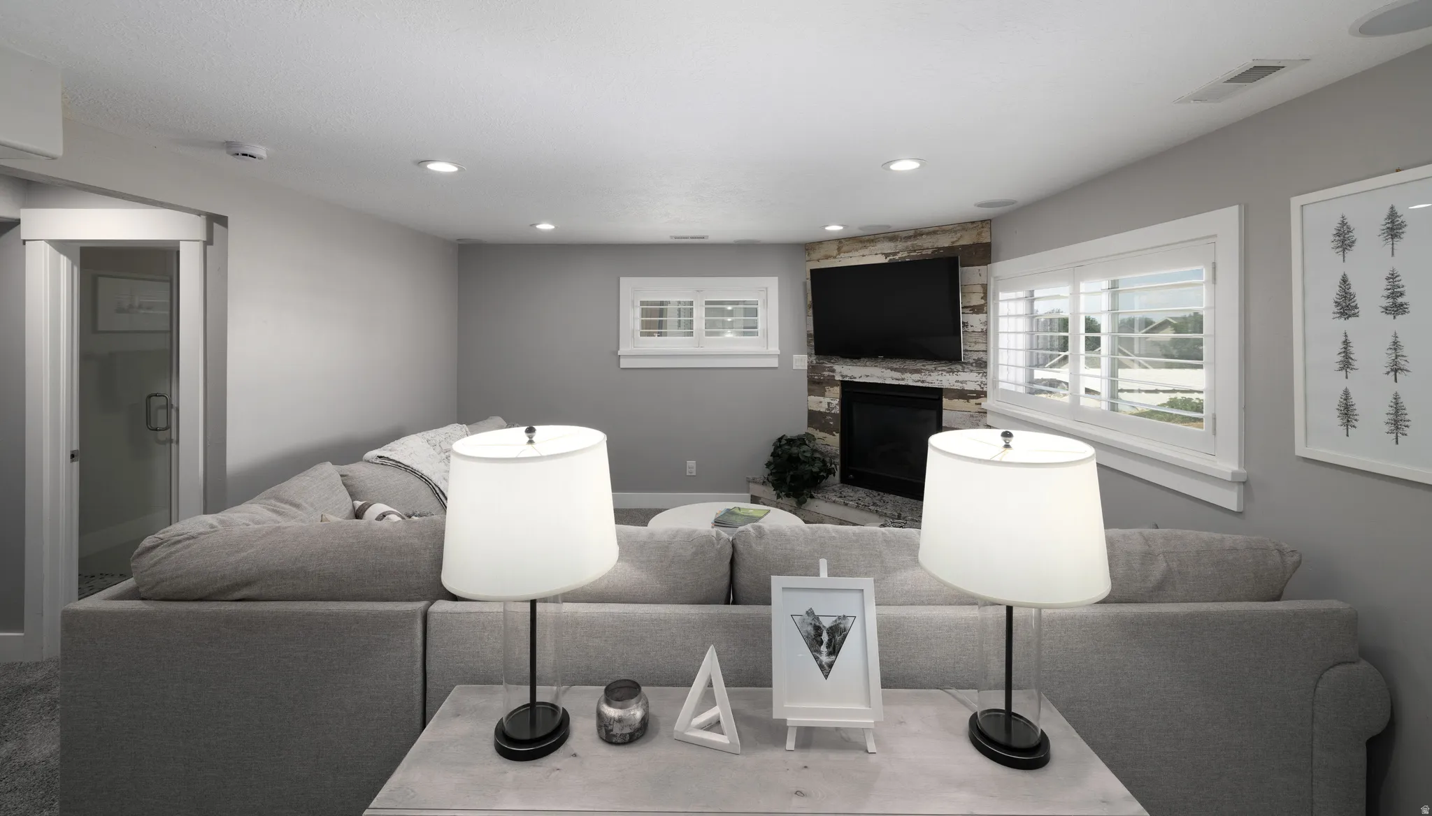 Stacked stone fireplace with media recess, recessed lighting, and white window shutters