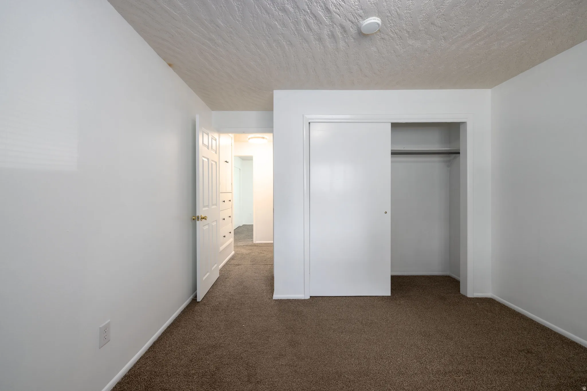Neutral wall paint with textured ceiling, brown carpet, and a sliding closet door