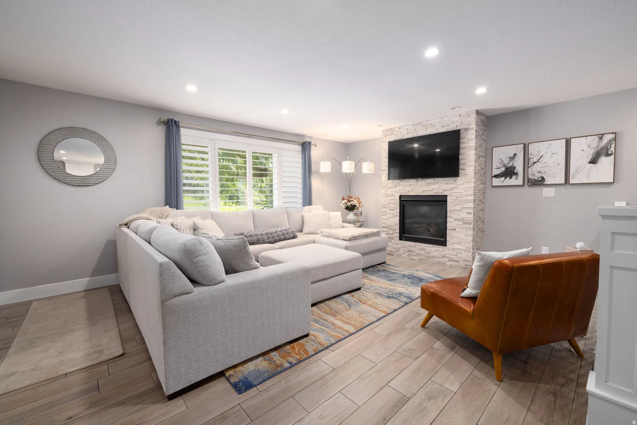 Recessed lighting, wood-finish flooring, and a fireplace with a stacked stone surround
