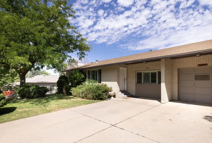 Brick exterior with an attached garage, paved driveway, and mature landscaping