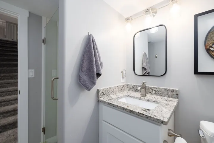 White vanity with a rectangular undermount sink, speckled countertop, and brushed nickel faucet