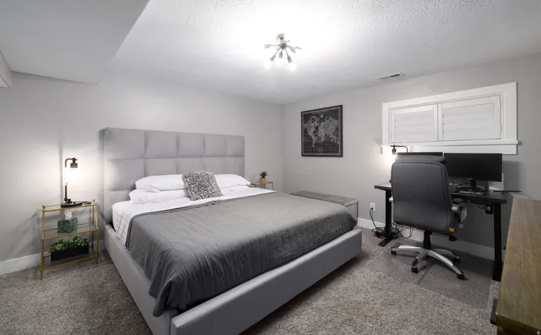 Neutral wall paint, textured carpeting, window with louvered shutters, and a ceiling-mounted light fixture