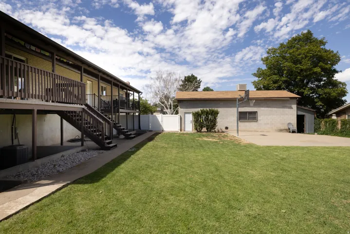 Expansive backyard featuring a manicured lawn, multi-level deck with wood railings, and a detached structure with a basketball hoop