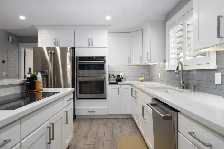White shaker cabinetry with stainless steel hardware, wood-finish flooring, undermount sink, built-in stainless steel appliances, and a gray subway tile backsplash