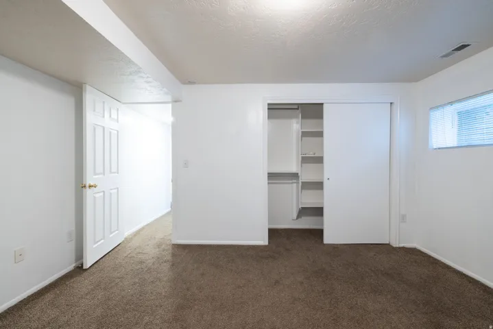 Carpeted room featuring a built-in closet with shelving and sliding doors, a white paneled door, and a horizontal window with blinds