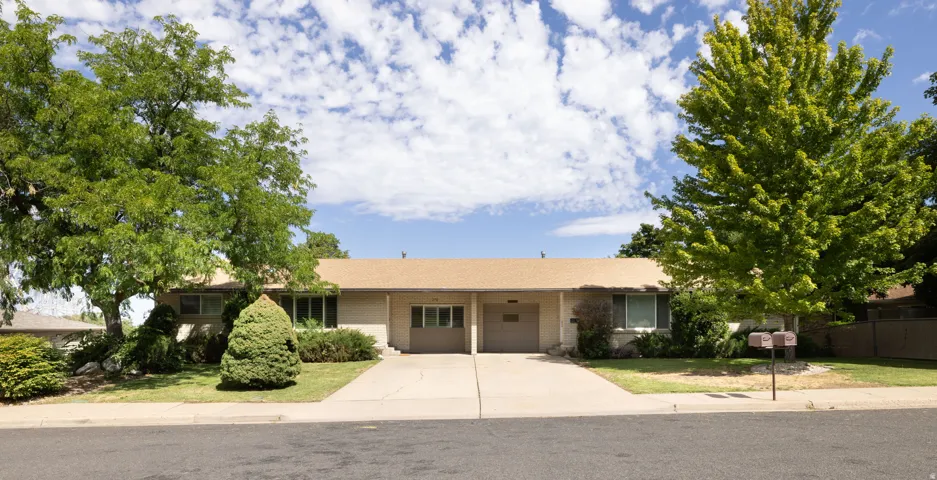Ranch-style exterior with a low-slope roof, two single-car garages, and a front yard featuring mature trees and established landscaping