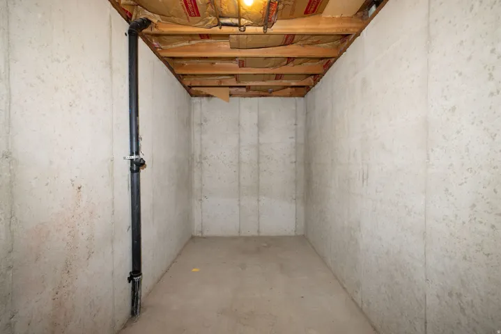 Exposed wooden ceiling joists, concrete walls, concrete flooring, and visible utility piping