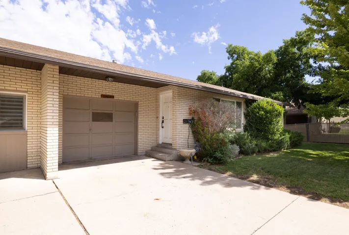 Brick exterior with an attached garage, concrete driveway, and established landscaping