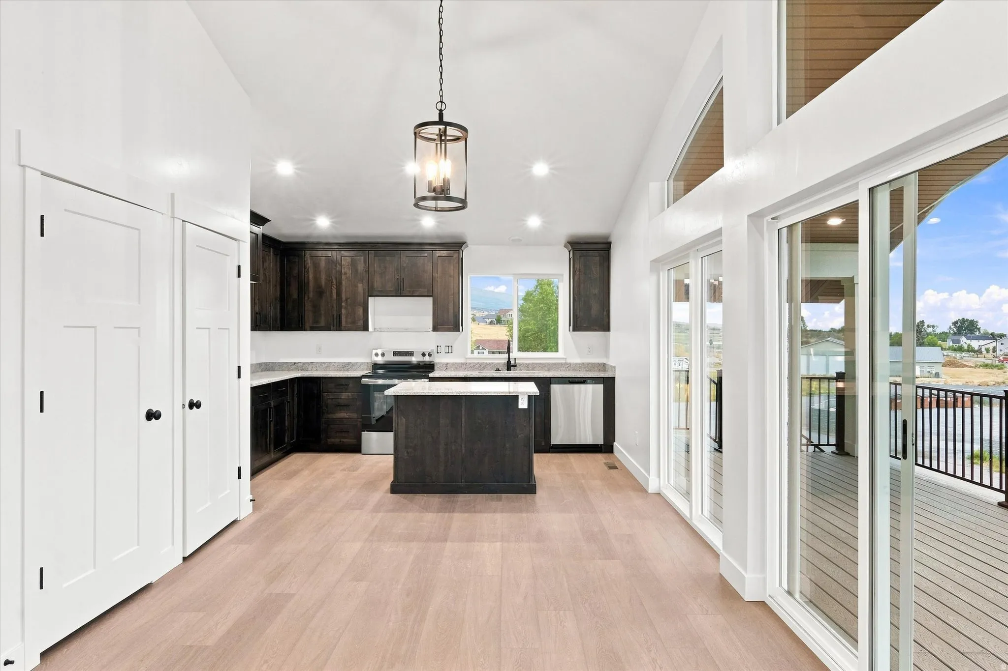 Open-concept space featuring wood-finish flooring, dark wood cabinetry, a central kitchen island, and high ceilings with recessed lighting