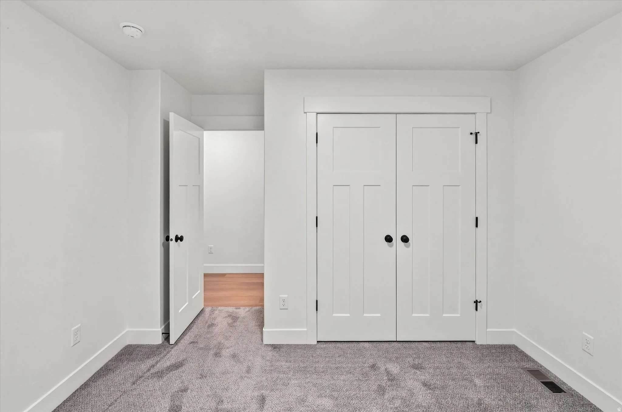 Neutral white walls and trim, gray carpet flooring, and white paneled doors with black hardware