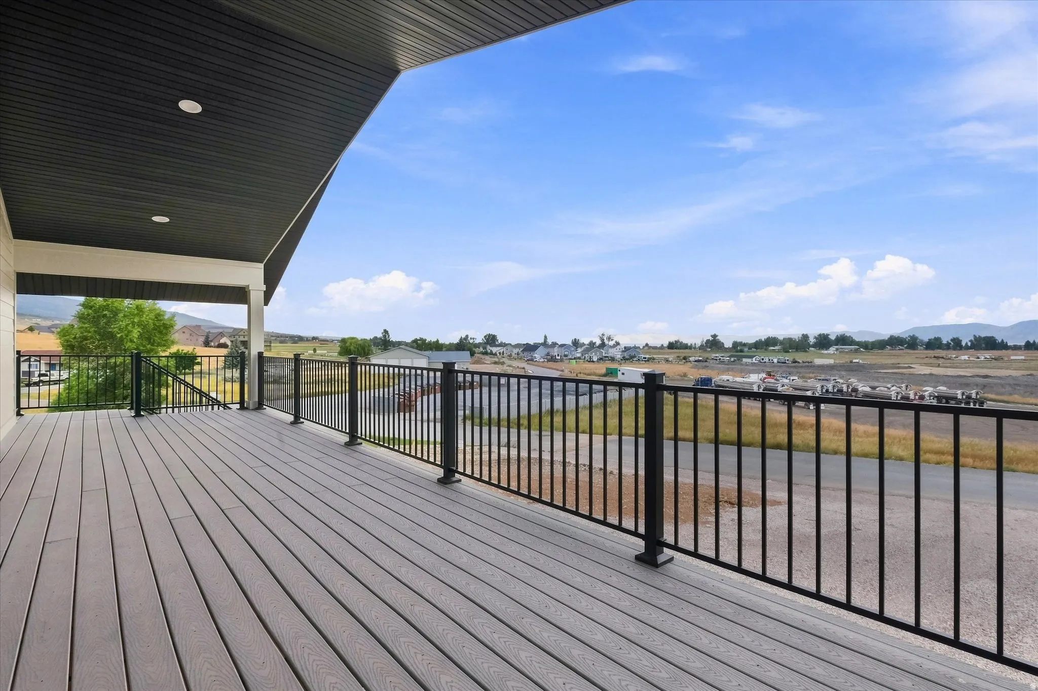 Expansive outdoor deck with composite decking and black metal railings, featuring a covered area with recessed lighting