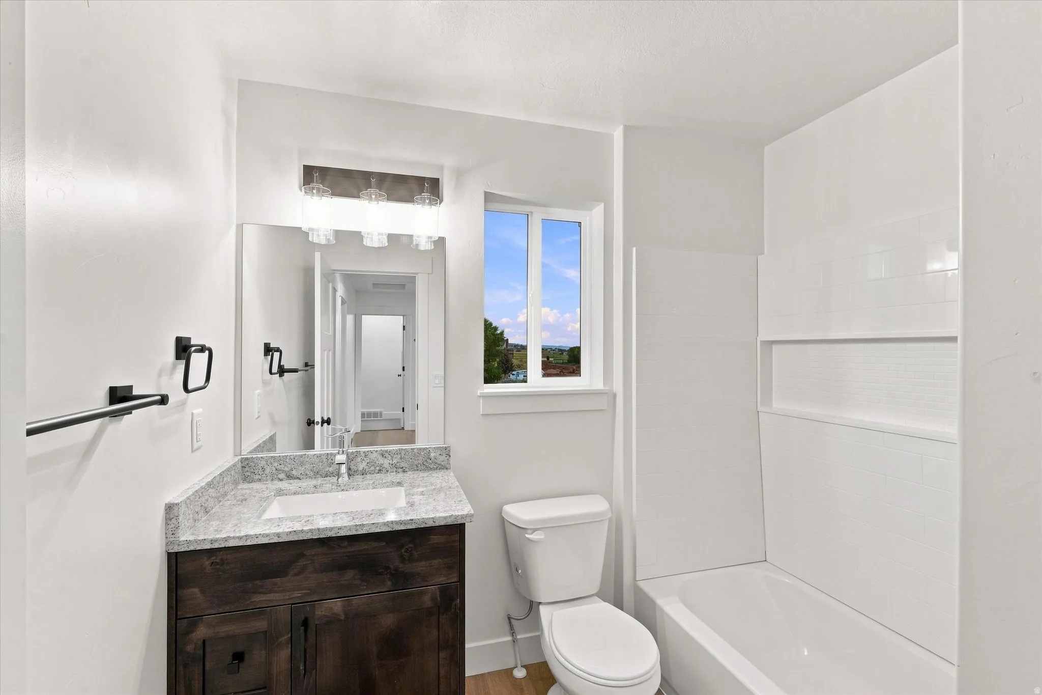 Bathroom featuring a wood-finish vanity with a stone countertop, an undermount sink, and a built-in bathtub with a tiled surround