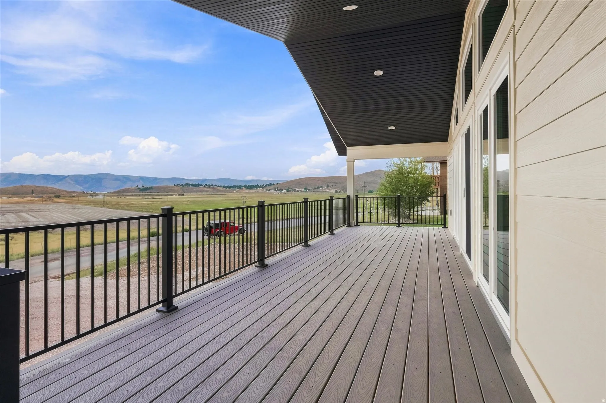 Expansive outdoor deck featuring wood-finish flooring, black metal railings, and a dark soffit with recessed lighting
