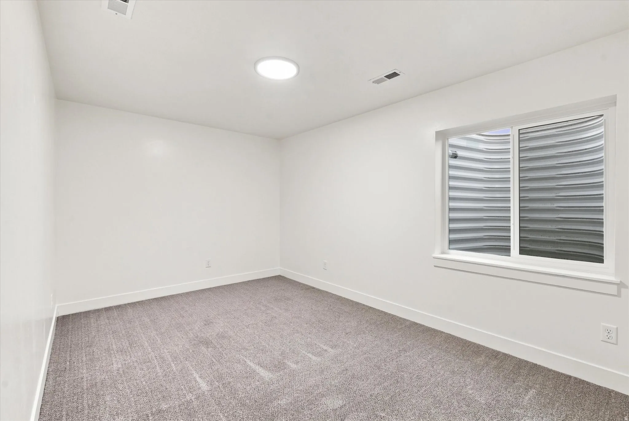 Recessed ceiling light, white painted walls, carpeted flooring, and a single window with white trim