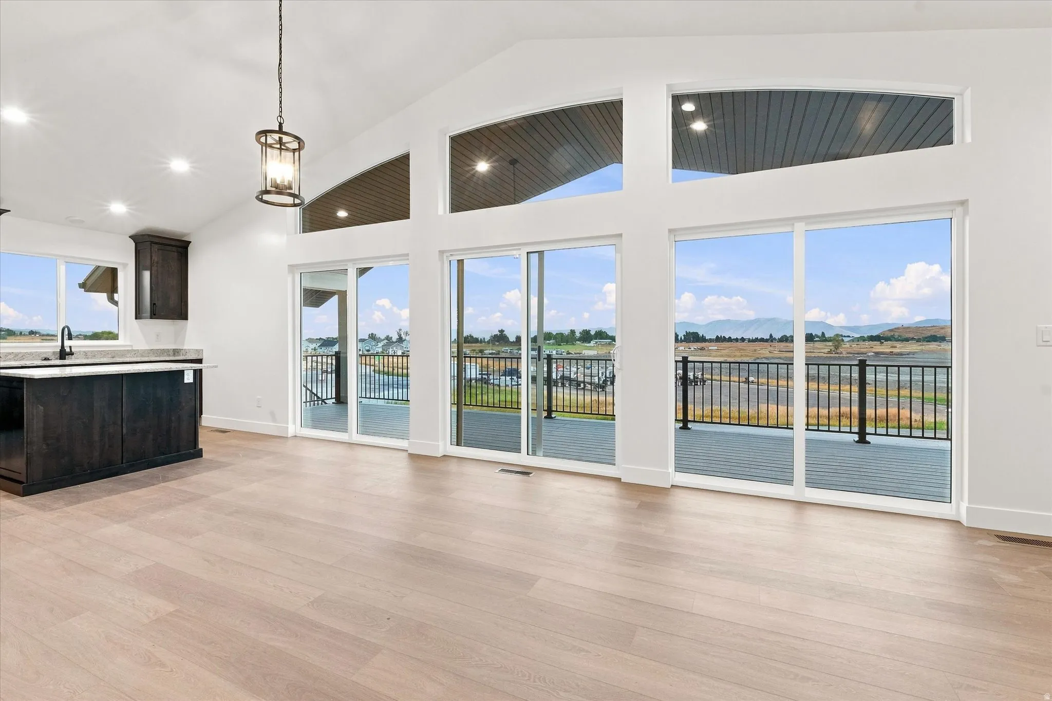 Vaulted ceilings with recessed lighting, light wood-finish flooring, dark wood cabinetry with light countertops, and multiple sliding glass doors leading to an exterior deck with a black railing