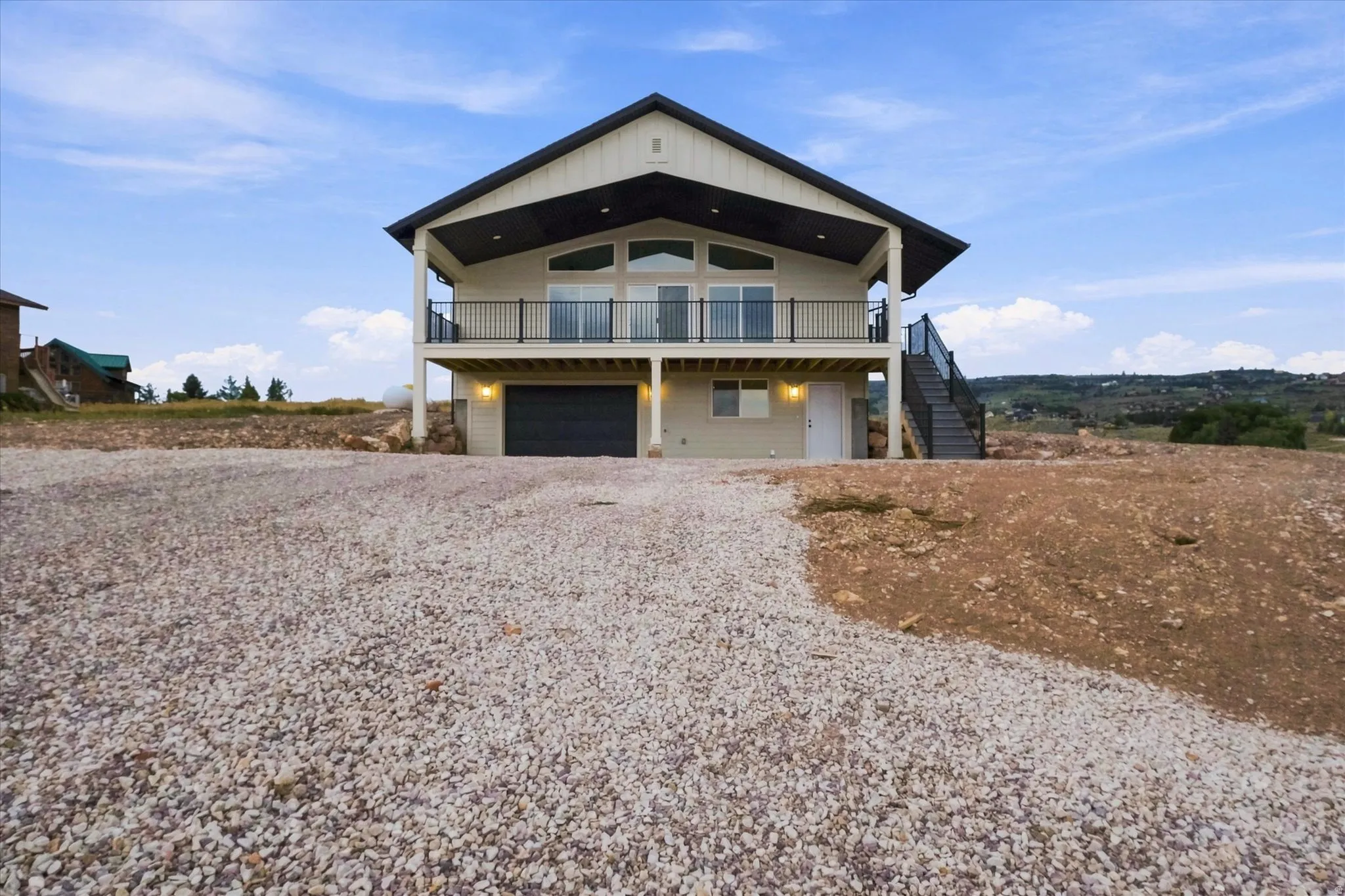 Two-story residence featuring a large upper-level balcony with a black railing, a lower-level garage with a dark door, and an exterior staircase