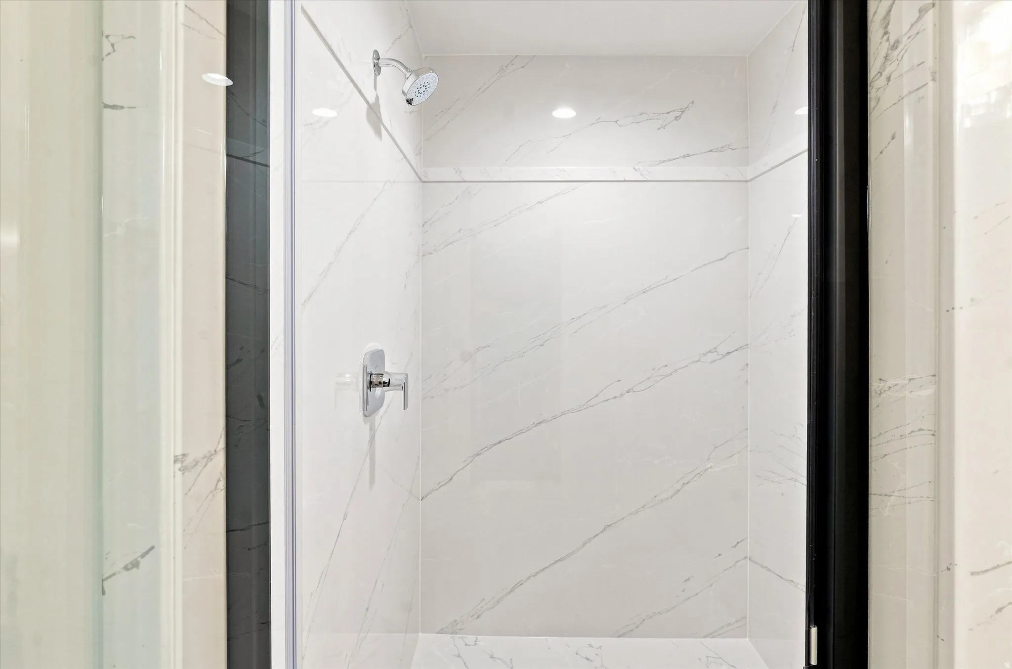 Walk-in shower featuring white stone-look wall tiling, a chrome shower head, and a chrome mixer tap