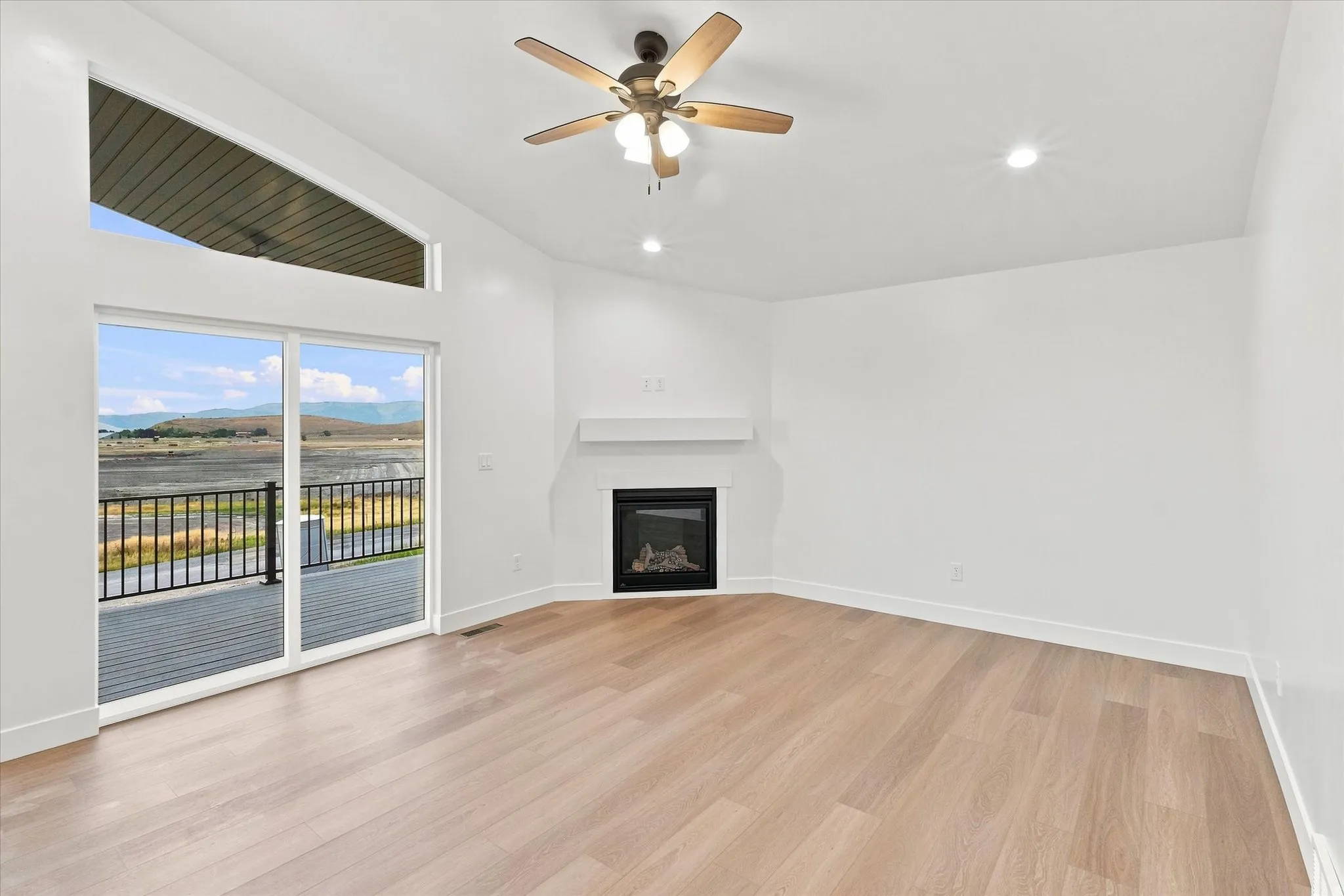 Vaulted ceiling with an integrated ceiling fan, recessed lighting, wood-finish flooring, and a fireplace with a white mantle