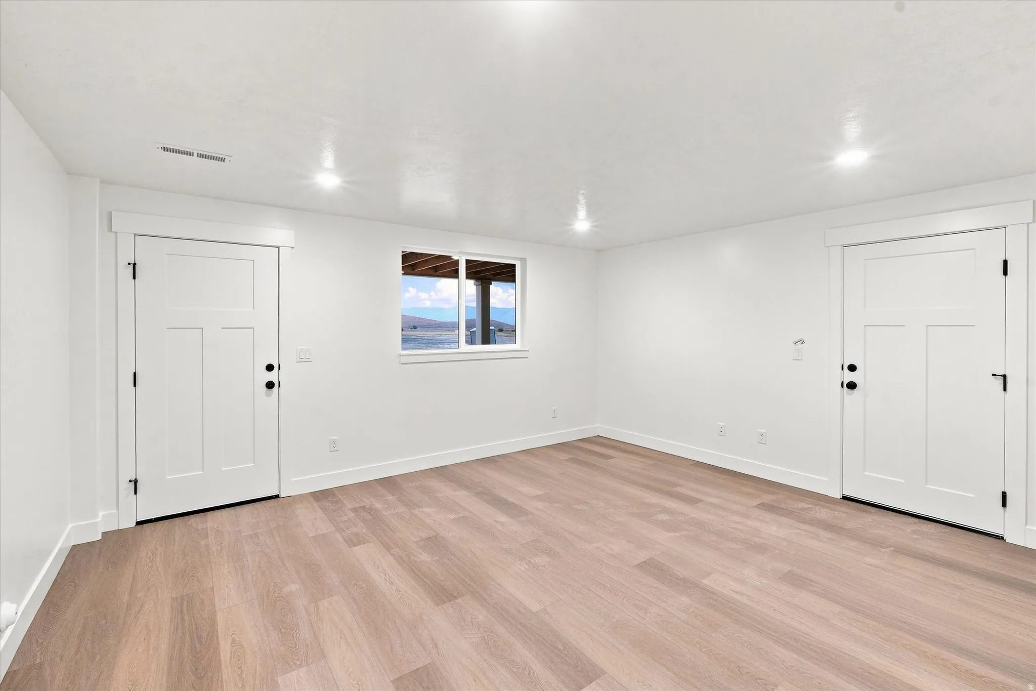 Light wood-finish flooring, recessed lighting, white trim, and a window offering a distant landscape