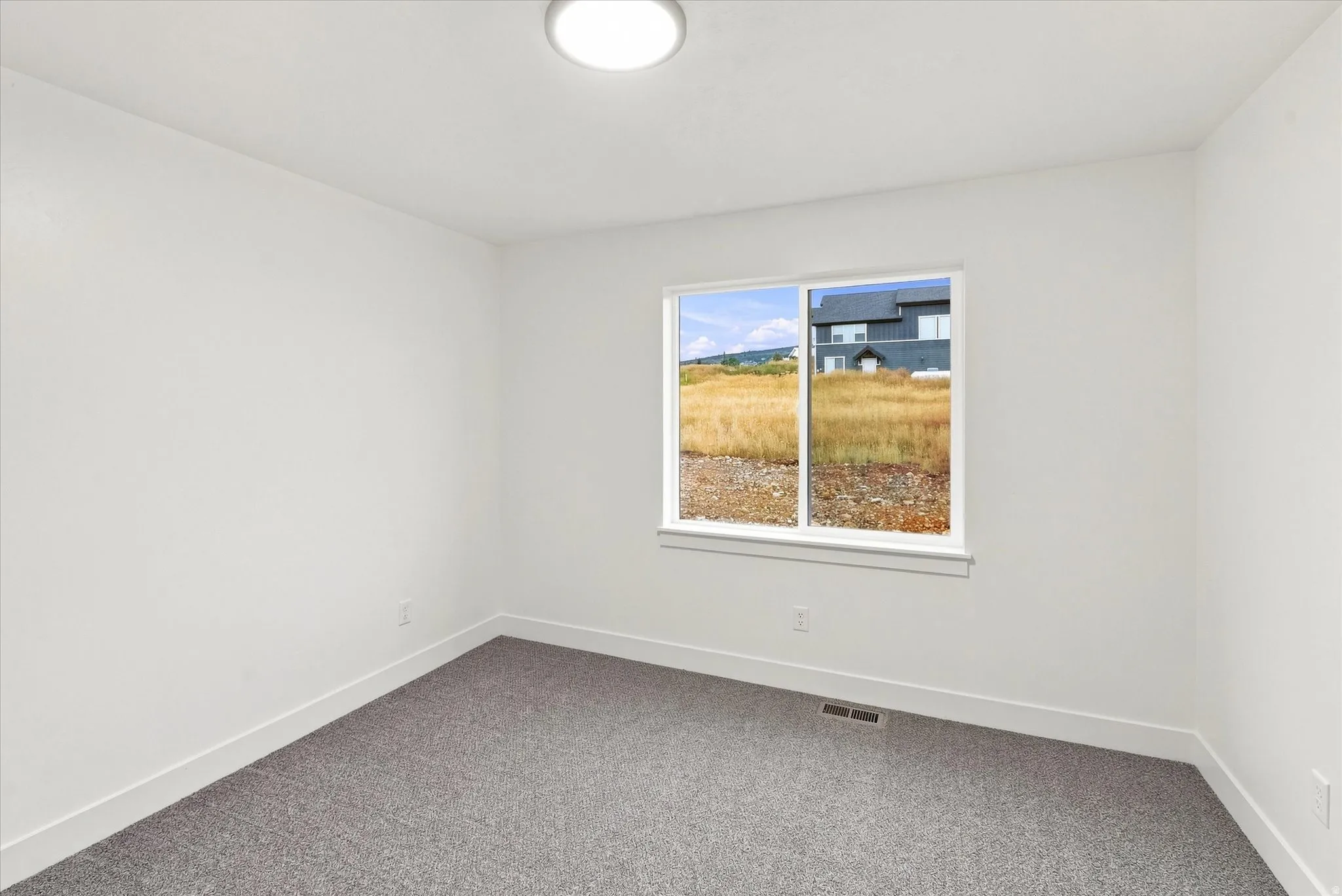 Bright interior room featuring a large window, white walls, and gray carpet