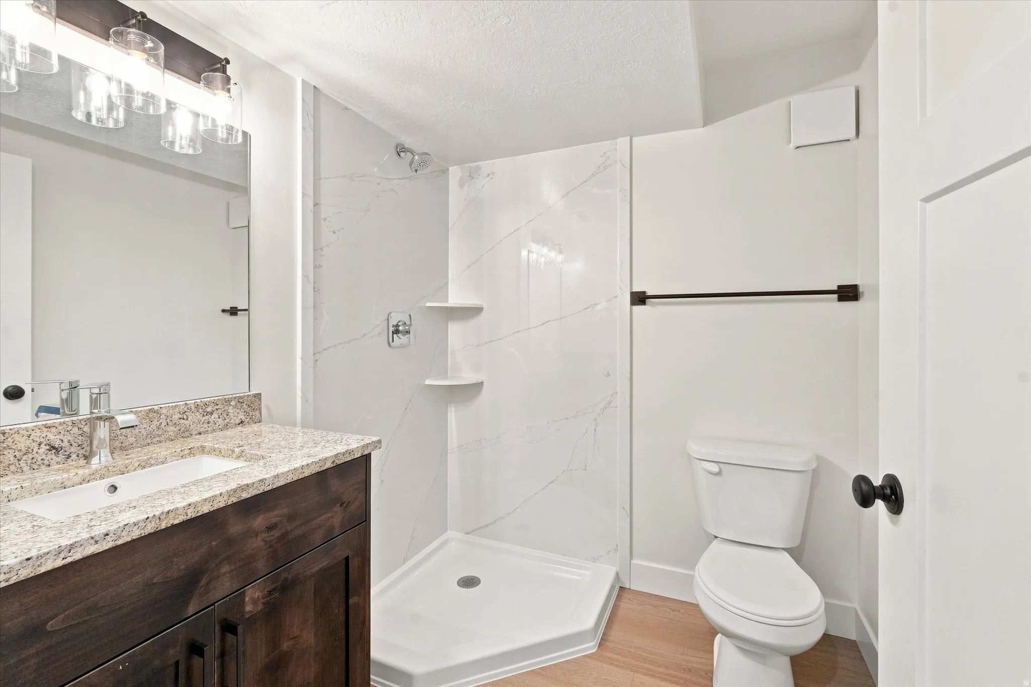 Bathroom featuring a wood-finish vanity with a granite countertop, undermount sink, and a walk-in shower with a white tiled surround