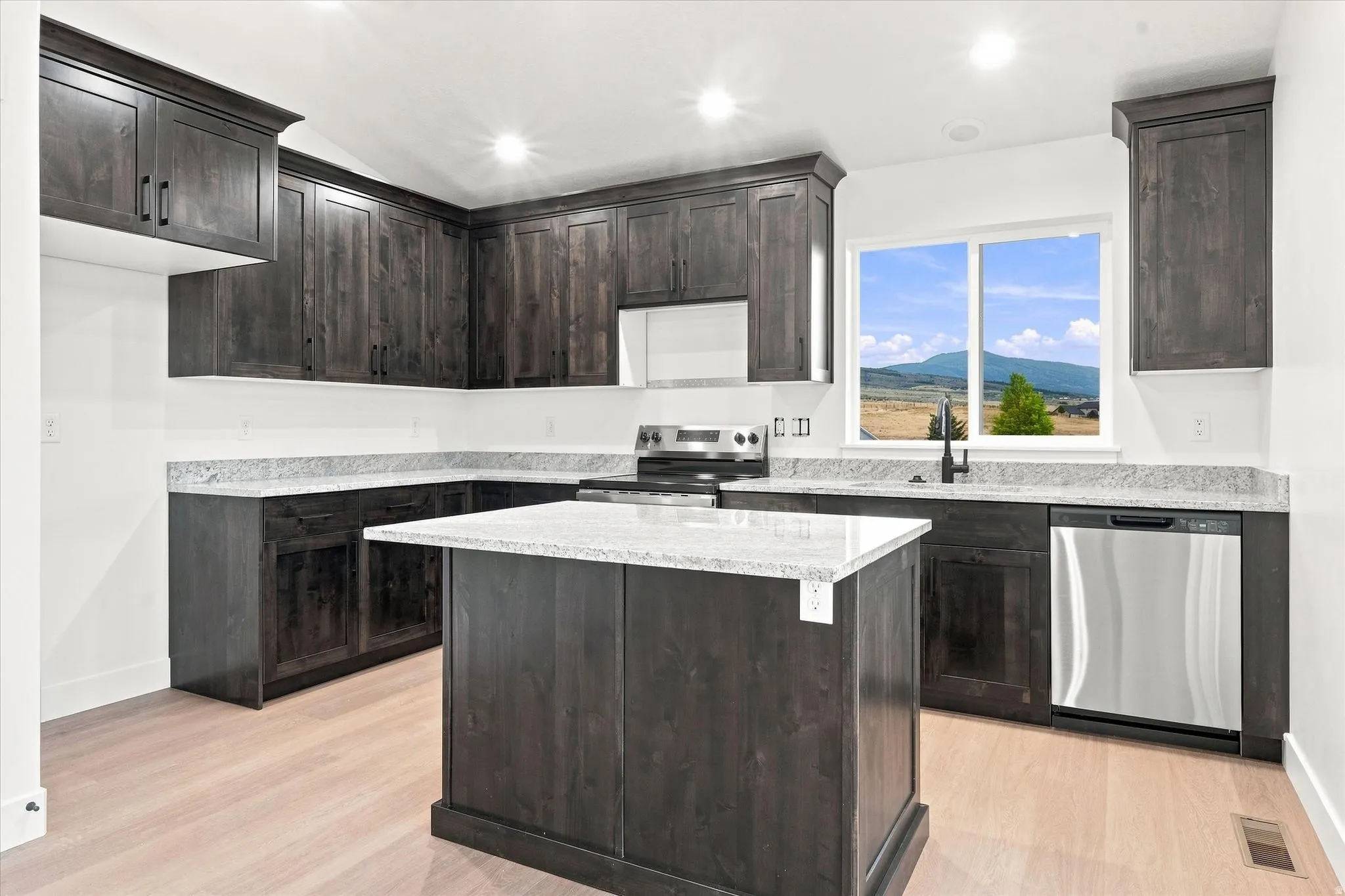 Kitchen featuring an island, dark wood-finish cabinetry, light-toned countertops, stainless steel appliances, and wood-finish flooring