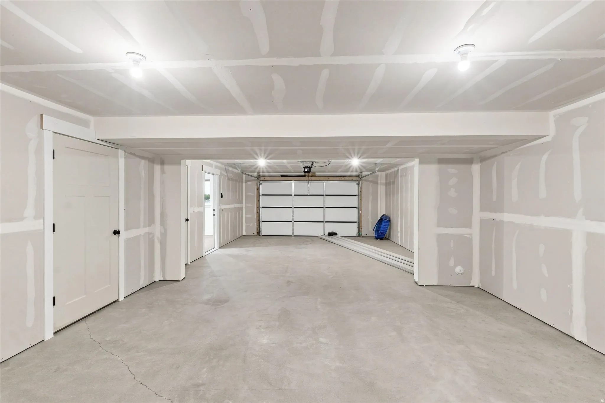 Concrete flooring, unfinished drywall, two panel doors, overhead lighting, garage door