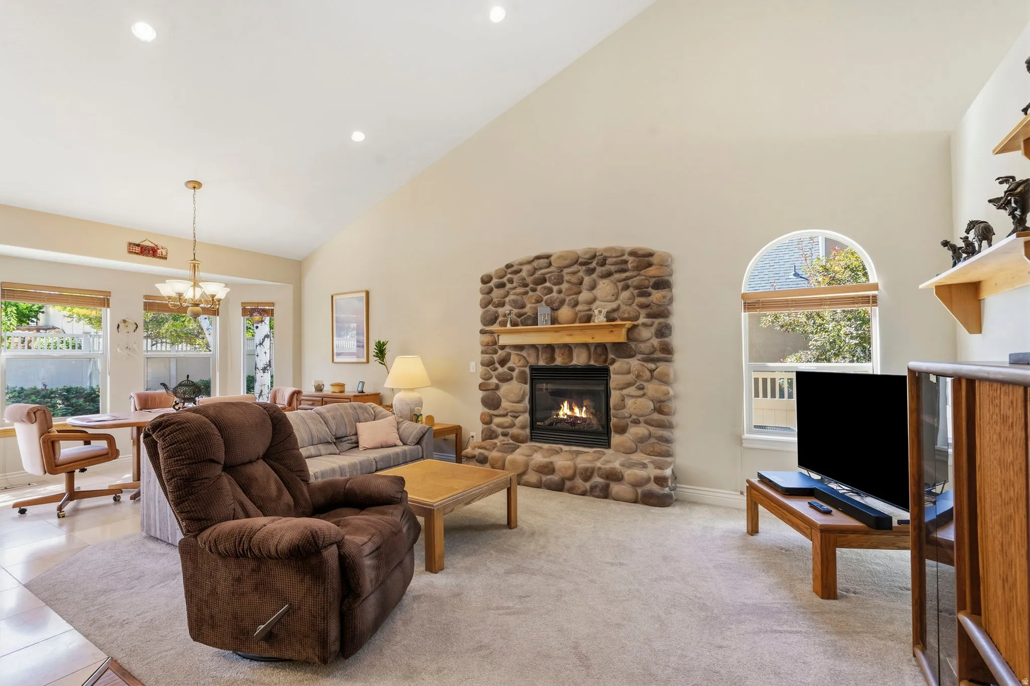 Vaulted ceilings, recessed lighting, stone-clad fireplace with wood mantel, multiple windows, and arched window accent