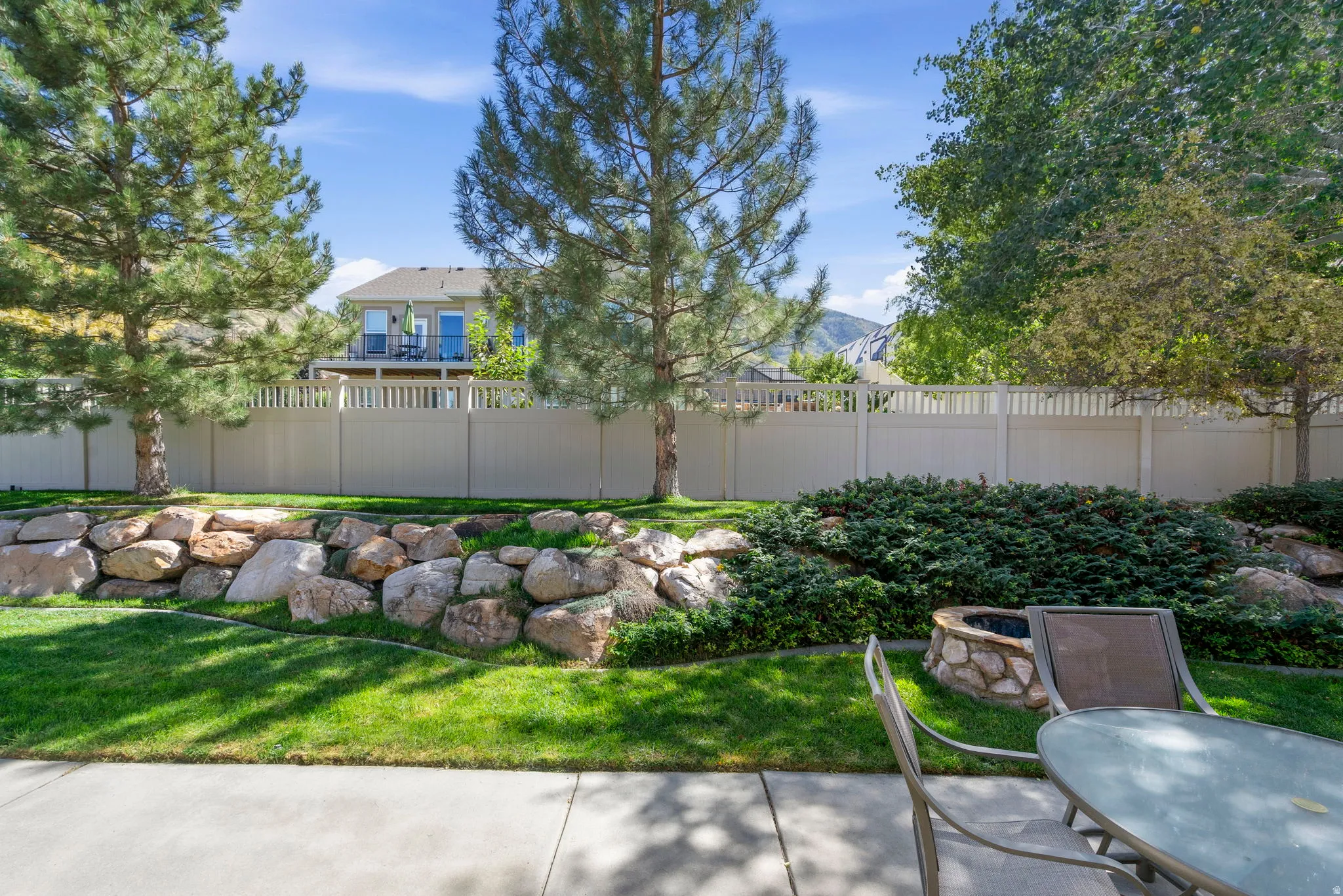 Concrete patio with rock-lined built-in fire pit, surrounded by lush green lawn