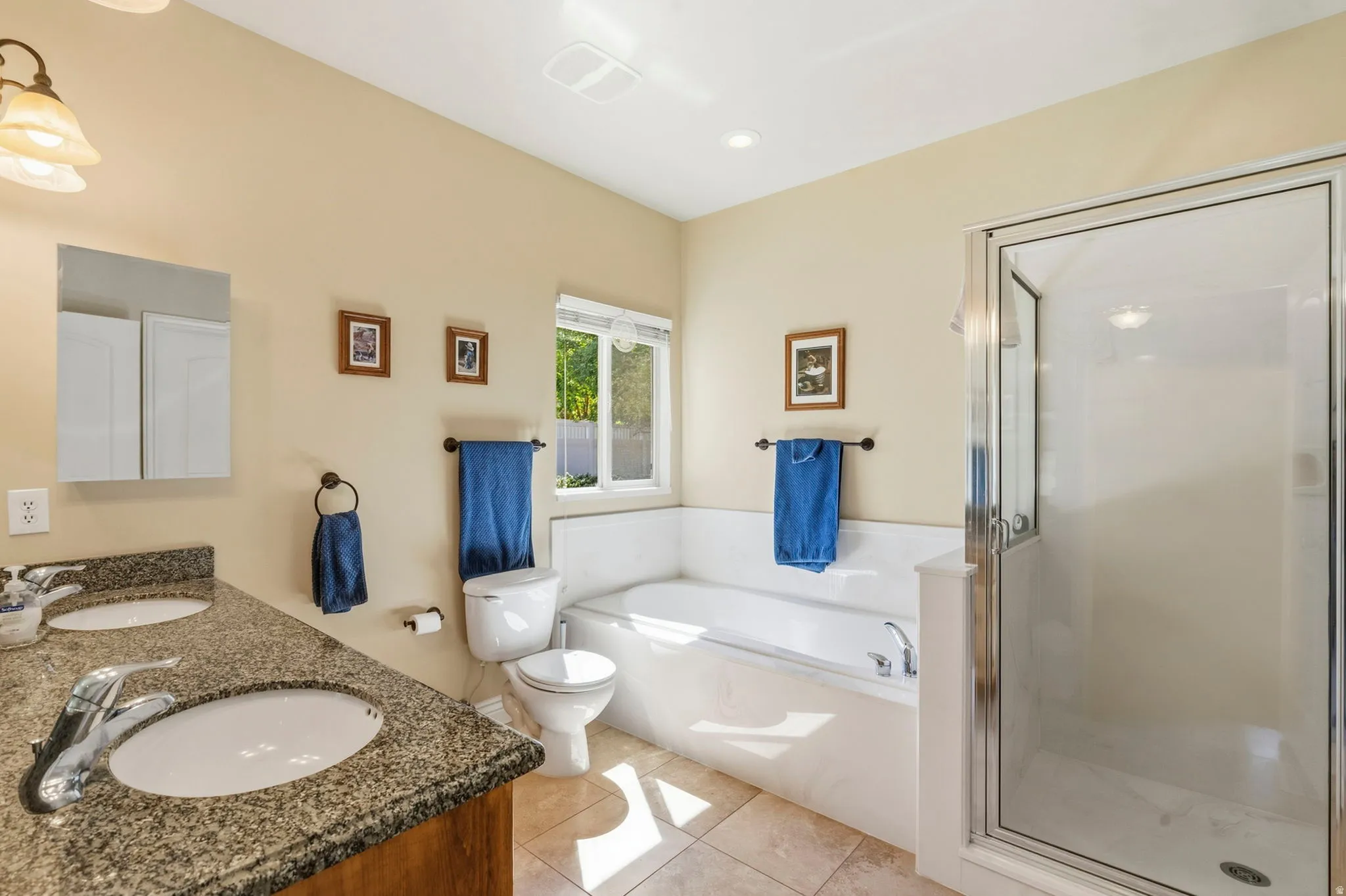 Dual vanity with undermount sinks and granite-finish countertop, built-in soaking tub, separate glass-enclosed shower, and tiled flooring