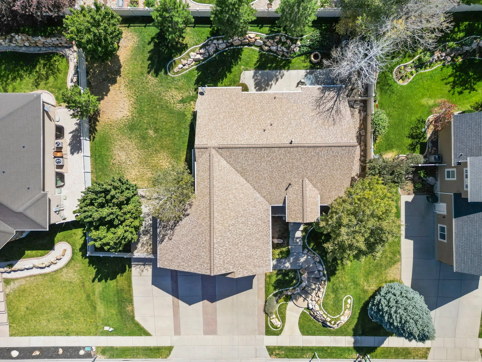 Pitched roofline residence with a concrete driveway, mature landscaping, and an expansive lawn