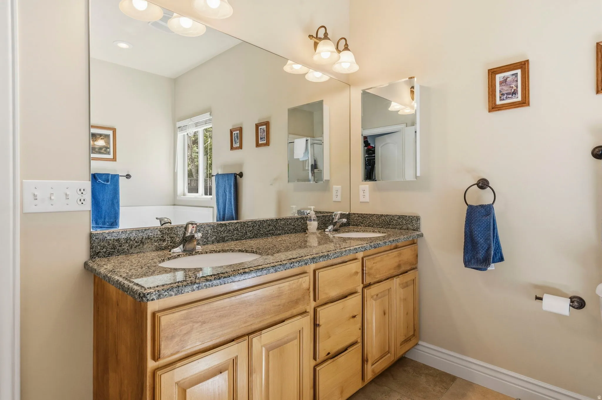 Dual vanity with light wood cabinetry, granite countertop, and undermount sinks