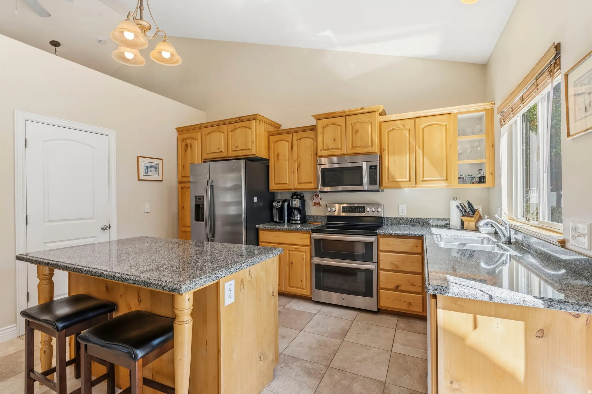 Kitchen featuring a vaulted ceiling, wood cabinetry, stainless steel appliances, granite countertops, and tile flooring