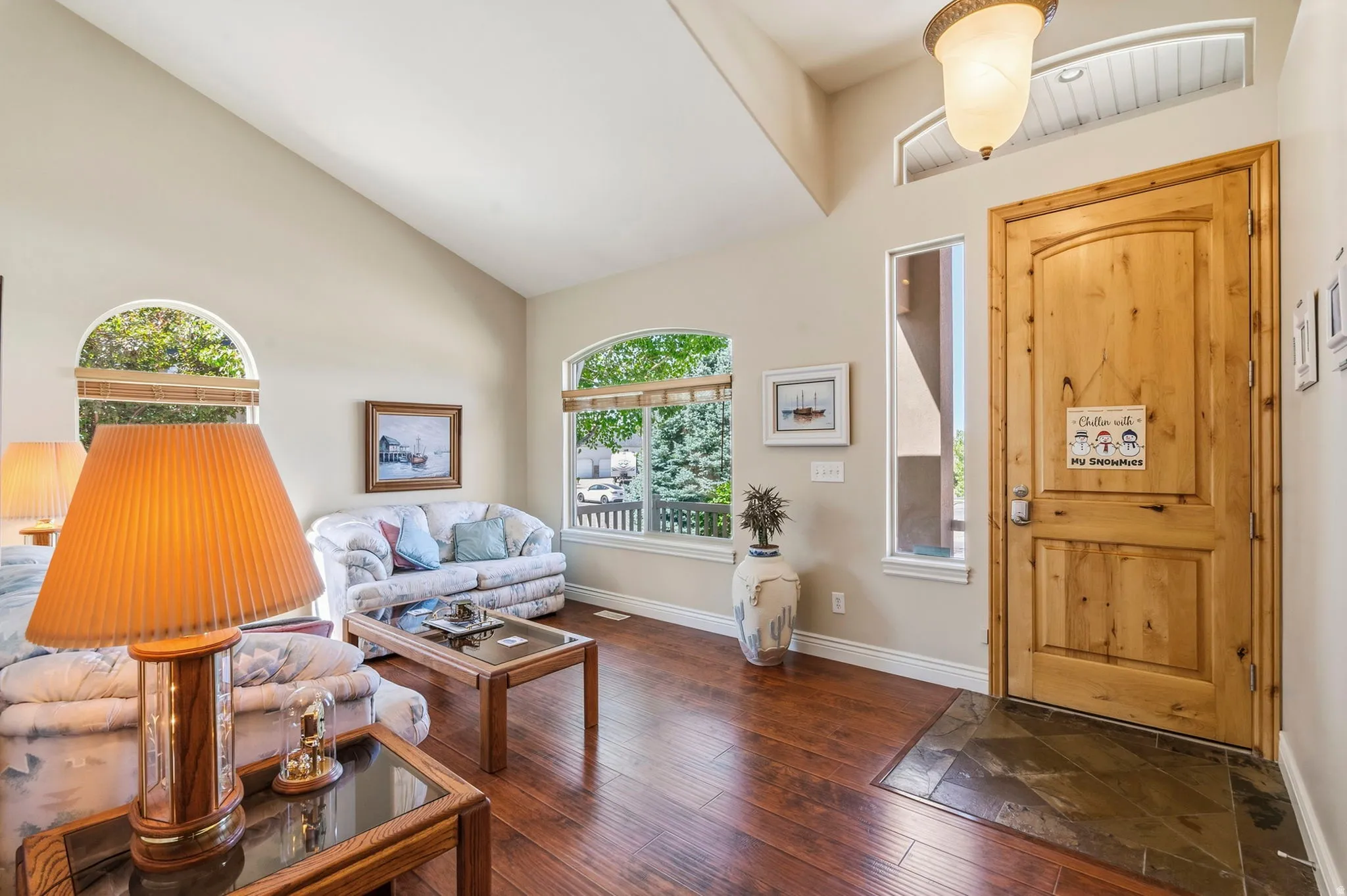 Vaulted ceiling with an arched transom window, natural wood-finish door, tile entry, and wood-finish flooring