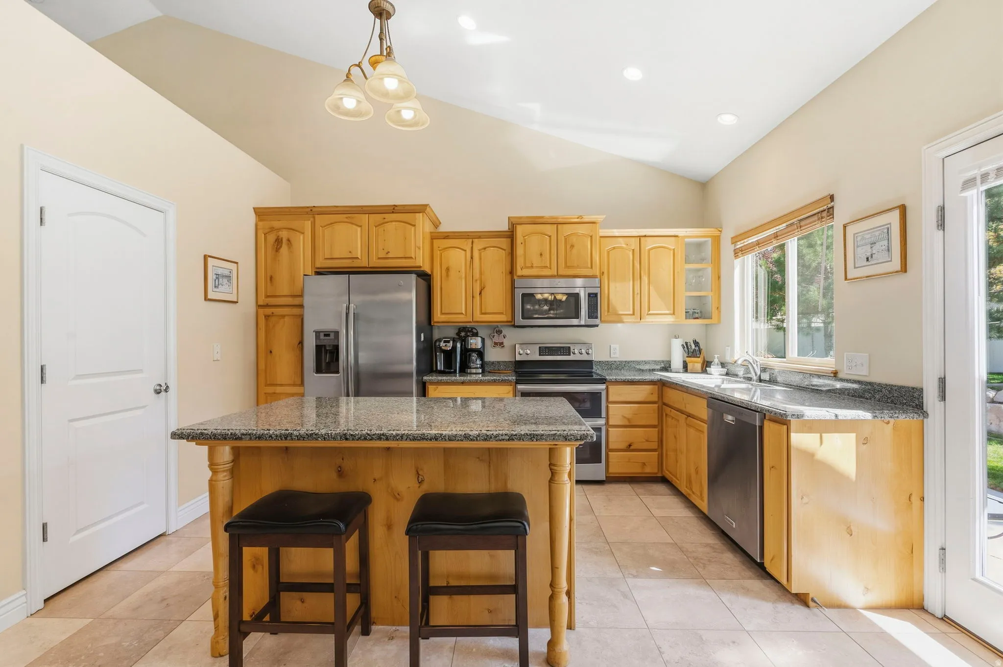 Vaulted ceiling with recessed lighting, wood cabinetry, granite-finish countertops, stainless steel appliances, and a kitchen island with seating
